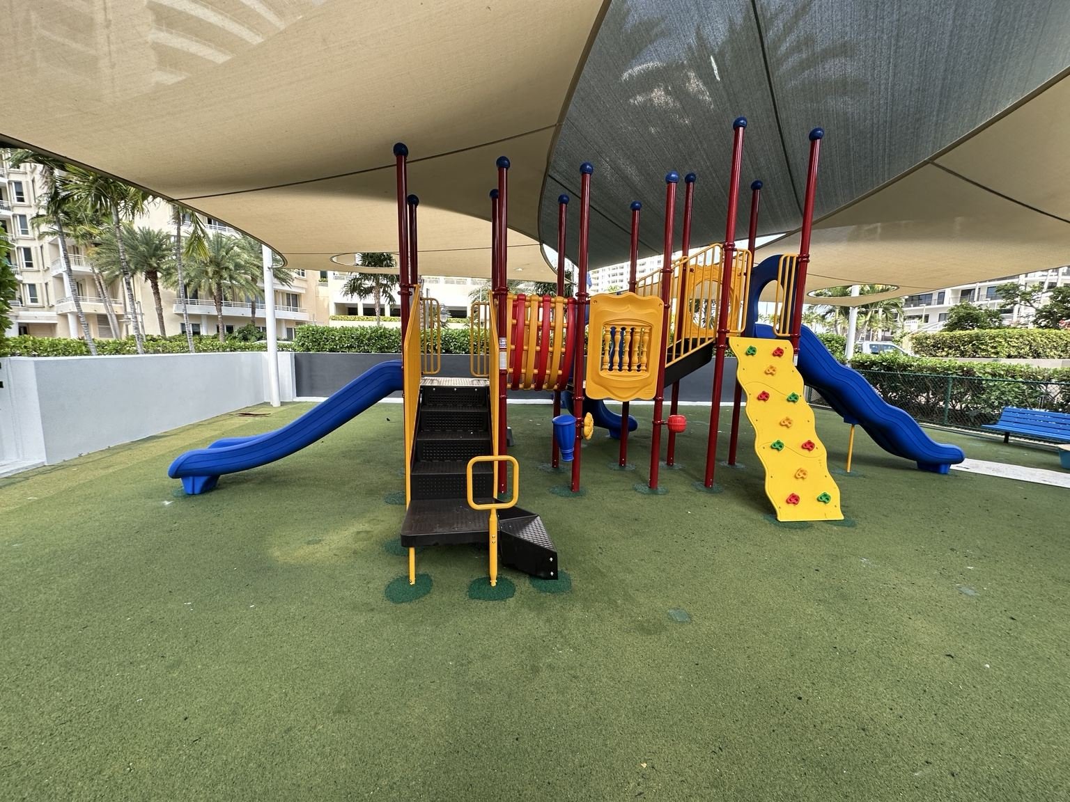 Shaded commercial playground structure with slides and climbing features, installed under large shade sails.